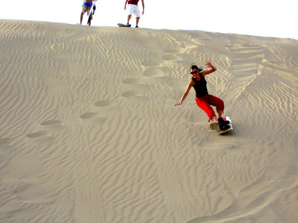 Personas practicando sandboarding en las dunas del desierto de la Huacachina