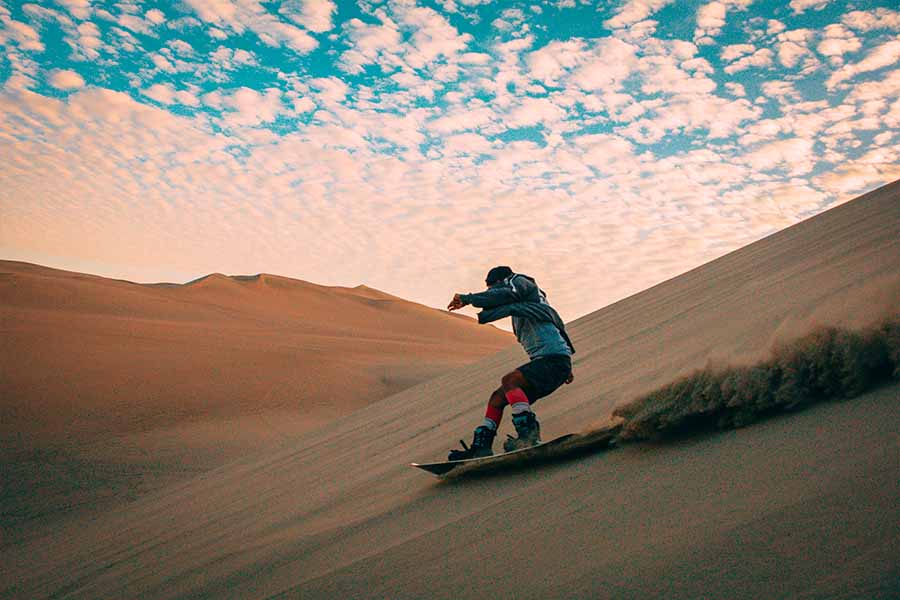 Turista practicando sandboarding en las dunas del desierto de Paracas, cerca de las Islas Ballestas.